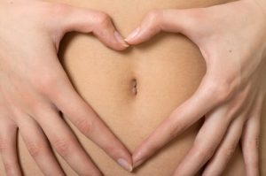womans hand forming a heart symbol around navel